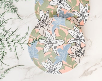 Könnte beinhalten: Zwei runde Teller mit einem floralen Design. Die Teller sind rosa mit grünen Blättern und weißen und blauen Blumen.