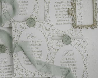 Könnte beinhalten: Hochzeitstischplan mit floralem Muster. Jede Karte zeigt Namen und eine Nummer, verziert mit Wachssiegeln und einem Band. Ein Rahmen im Vintage-Stil ist ebenfalls vorhanden.