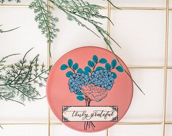 May include: A pink round ceramic coaster with a floral design and the text "truly grateful".