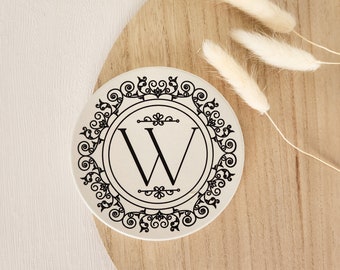 Könnte beinhalten: Weißer Keramikuntersetzer mit einem schwarzen, verzierten Design mit dem Buchstaben "W" in der Mitte.