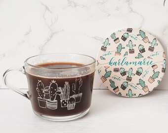 May include: A glass mug with a black coffee inside and a cactus design. The mug is next to a round coaster with a cactus pattern and the text "karlamarie" in blue cursive.
