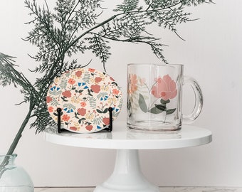 Könnte beinhalten: Ein weißer Kuchenständer mit einer Tasse mit Blumenmuster und einem Untersetzer mit Blumenmuster darauf. Der Untersetzer steht auf einem schwarzen Ständer.