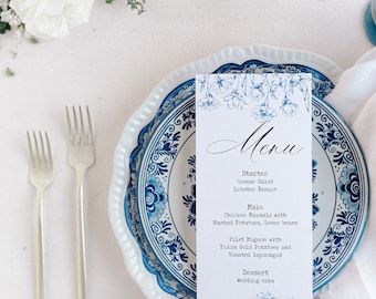 May include: A formal table setting with a menu card, two forks, and a decorative plate. The menu card features floral illustrations and the word "Menu". The plate has a blue and white floral design. White flowers are in the background.