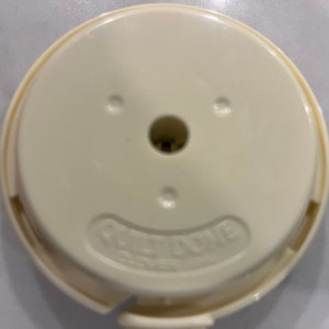 May include: A white plastic round lid with a small hole in the center and the text "RE-TAPE" printed on the bottom.