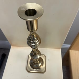 May include: A gold metal candlestick with a round top and a decorative base. The candlestick is made of a shiny metal and has a classic design.