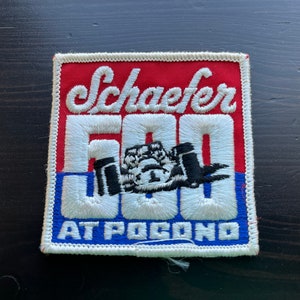 May include: A red, white, and blue embroidered patch with the text "Schaefer 500 at Pocono" and a black and white image of a race car.