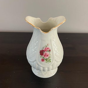 May include: White ceramic vase with a gold rim and a floral design featuring pink and red roses.