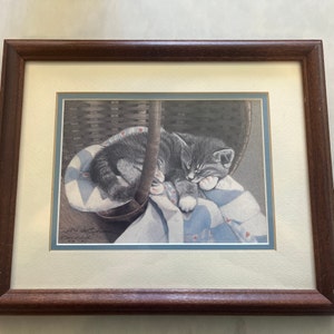 May include: A framed print of a gray and white kitten sleeping in a basket. The kitten is curled up on a blue and white quilt with its paws tucked under its chin. The print is signed "Jina K. Edwards" and dated "2003".