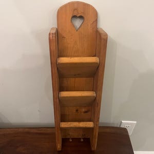May include: Wooden wall-mounted organizer with three shelves and a heart-shaped cutout. The natural wood has a warm tone. The shelves are spaced to hold mail or small items. A rustic, country-style decor piece.