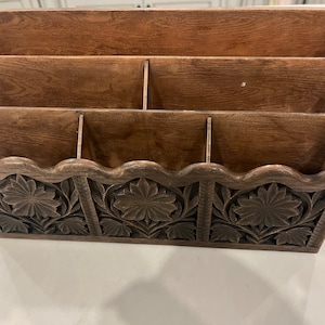May include: A wooden desk organizer with five compartments and a carved floral design. The organizer is brown and has a scalloped edge.