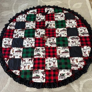 May include: A red and green plaid Christmas tree skirt with a black lace trim. The skirt is made of patchwork fabric with various designs featuring the words "Georgia Bulldogs" and "Hangin' with the Dawgs".