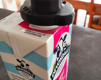 May include: A black plastic milk carton spout cover with the word "SIGG" printed on it. The cover is on top of a carton of Devondale Light Full Cream Milk. The carton has a blue and white striped design with a cow illustration and the text "Devondale Australian Dairy".