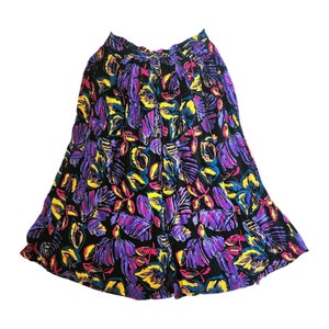 Puede incluir: Una falda negra con estampado floral de colores. El estampado presenta flores moradas, amarillas, rosas y azules sobre un fondo negro.