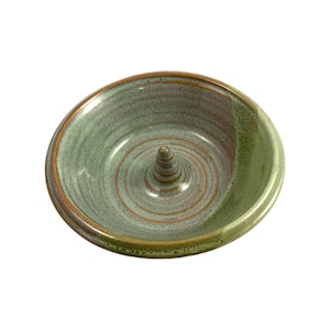 Puede incluir: Un sacacorchos de manzana de cerámica verde y marrón con un centro elevado. El sacacorchos está diseñado para quitar el corazón de una manzana.