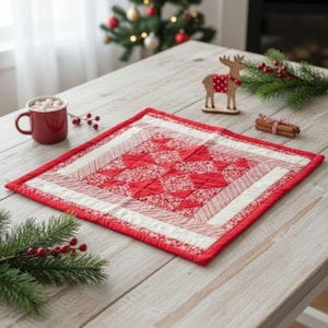 May include: A square, quilted Christmas placemat with a red and white pattern. The center features a patchwork design of red floral fabric and red triangles. The border is white and red striped, with a solid red edge. The placemat is on a wooden table.