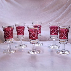 Puede incluir: Juego de seis copas de licor vintage. Cada copa presenta un cuenco transparente con interior rojo rubí y borde dorado. El exterior está decorado con un patrón de diamantes en rojo rubí. Tallo y base transparentes.
