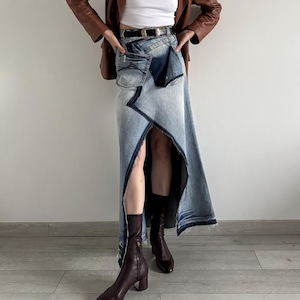 May include: A woman wearing a brown leather jacket, a white vest top, a blue denim skirt, and brown heeled boots.