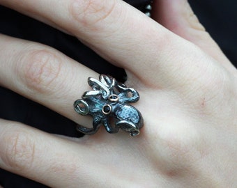 Peut inclure: Une bague en argent en forme de pieuvre avec des accents noirs et de petites pierres précieuses violettes pour les yeux.