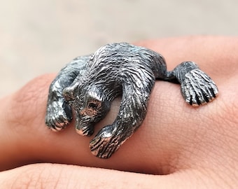 May include: A silver ring featuring a detailed bear sculpture. The bear is depicted in a crouching position with its paws outstretched.