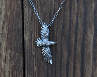 May include: A silver pendant necklace featuring a detailed, stylized bird in flight. The pendant is attached to a silver chain.