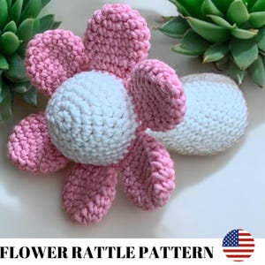 May include: A crocheted flower rattle toy with a white center and pink petals. The rattle is made of soft yarn and is perfect for babies to play with.