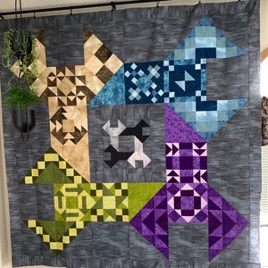 May include: A quilt with a geometric pattern in shades of blue, green, purple, and brown. The quilt is made up of squares and triangles, and the colors are arranged in a repeating pattern. The quilt is hanging on a wall.