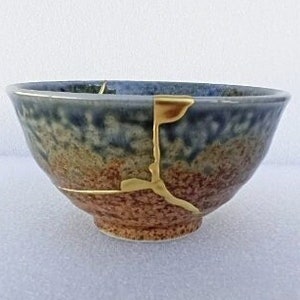 May include: A small, blue and brown ceramic bowl with a crack filled with gold paint. The bowl is slightly chipped on the rim.
