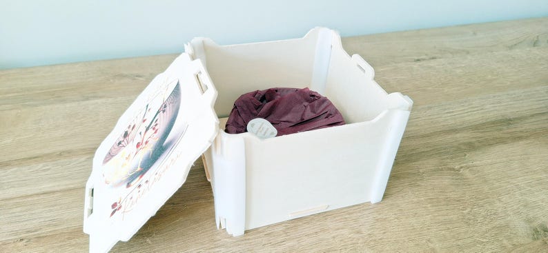May include: A white box with a hinged lid. The lid has a floral design and the words "Happy Birthday" printed on it. The box is open and a purple fabric item is inside.