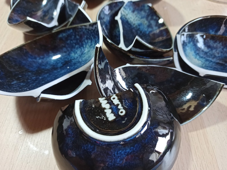 Puede incluir: Un juego de cuencos de cer&aacute;mica azul y blanca rotos con un borde blanco. Los cuencos tienen un esmalte moteado y est&aacute;n dispuestos en una pila.