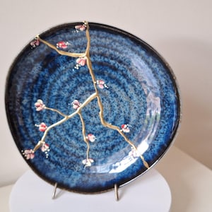 May include: A blue ceramic plate with a gold crackle glaze and a painted design of a cherry blossom branch with pink flowers.