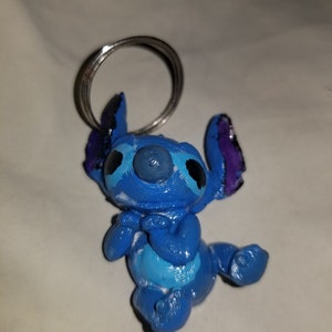 May include: Blue Stitch keychain with a silver ring. The Stitch figure is 3D printed and has a blue, purple, and white paint job.