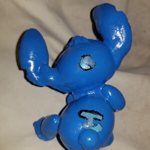 May include: Blue ceramic figurine of a cartoon character with large ears and a black outline of a number "626" on its back.