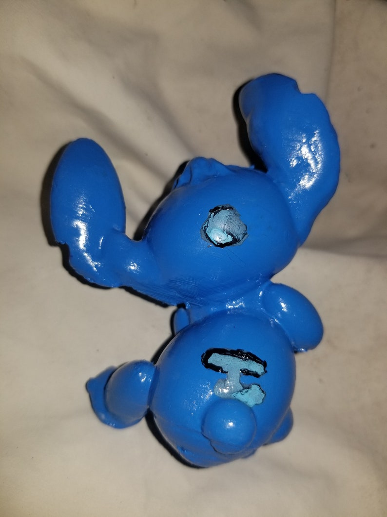 May include: Blue ceramic figurine of a cartoon character with large ears and a black outline of a number "626" on its back.