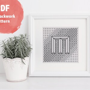 Könnte beinhalten: Schwarzweißes druckbares PDF-Muster für eine Blackwork-Stickerei mit dem Buchstaben "M". Das Design ist in einem weißen Rahmen gerahmt und an einer weißen Wand ausgestellt.