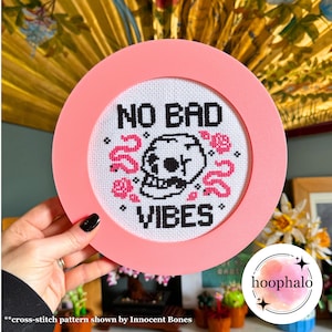 Könnte beinhalten: Rosa gerahmter Kreuzstich mit einem Totenkopf und dem Text "NO BAD VIBES".