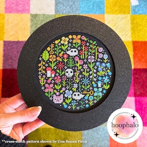May include: A black framed circular cross-stitch embroidery with a colorful floral design on a black background. The design includes flowers, leaves, mushrooms, keys, and skulls. The embroidery is framed in a black circle with a black background.