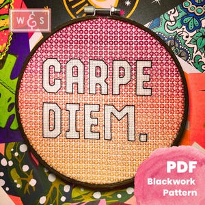 May include: A close-up of a round embroidery hoop with a blackwork cross-stitch pattern of the phrase "CARPE DIEM." The background is a gradient of red, orange, and yellow. The hoop is surrounded by colorful patterned paper.