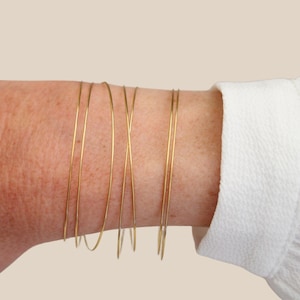 Peut inclure: Un ensemble de cinq bracelets en fil de fer doré empilés sur le poignet d'une personne.