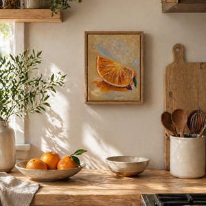 May include: A kitchen scene featuring a framed painting of an orange slice, a bowl of oranges, and various kitchen utensils. The painting has a wooden frame. The oranges are in a ceramic bowl. The scene has a warm, inviting aesthetic.