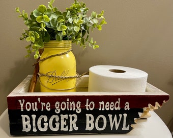 Puede incluir: Una caja de madera con un diseño pintado en rojo, negro y blanco. La caja tiene el texto "You're going to need a BIGGER BOWL" en la parte delantera. La caja contiene un rollo de papel higiénico y un tarro de vidrio amarillo con vegetación.