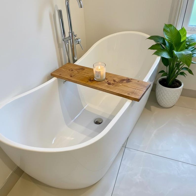 May include: A white, modern bathtub with a wooden bath tray holding a lit candle. A green plant in a white pot sits nearby. The tray is made of wood and is approximately 30 inches long.