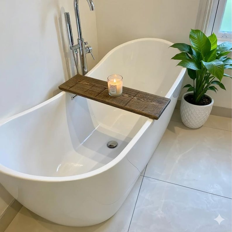 May include: A white, oval-shaped bathtub with a wooden bath tray holding a lit candle. A potted plant sits nearby. The wooden tray is rectangular and has a rustic, weathered appearance. The candle is in a clear glass container.
