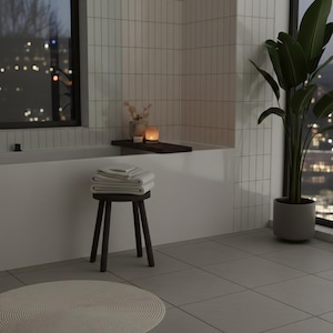 May include: A bathroom scene featuring a white bathtub, a dark wooden stool with folded white towels, and a large potted plant. A candle and decorative items sit on a wooden tray over the tub. The room has a modern, minimalist design with a city view.