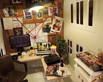 Puede incluir: Una habitación de casa de muñecas en miniatura ambientada como una oficina de detectives. La habitación tiene un tablero de corcho con fotos, mapas y notas, un escritorio con una computadora, una silla y una mesa auxiliar con libros y un juego de Clue.
