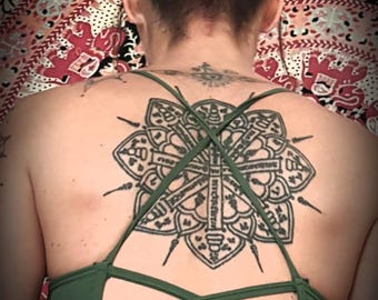 May include: A person with a large black and white tattoo on their back. The tattoo is a mandala design with intricate details. The person is wearing a green halter top with criss-cross straps in the back.