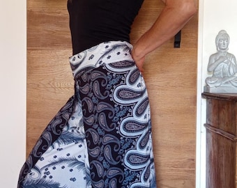 May include: Wide-leg palazzo pants with a black and white paisley and feather print. The pants are paired with a black tank top and white sandals. A straw hat with black stripes is also visible.