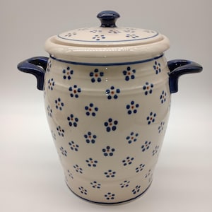 May include: A white ceramic jar with a blue and brown floral pattern and two blue handles. The jar has a lid with a knob on top.