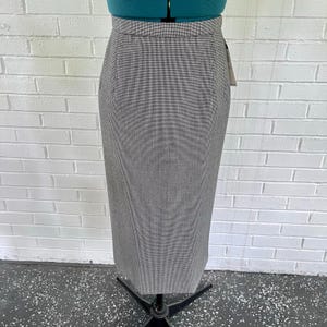 May include: A gray and white houndstooth pattern pencil skirt. The skirt is displayed on a dress form. The skirt has a high waist and a straight, knee-length cut. A tag is attached to the skirt.