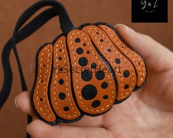 May include: A brown leather pumpkin-shaped keychain with black stitching and black polka dots. The keychain has a black leather strap.