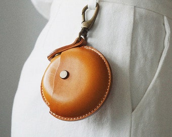 May include: A small, round, brown leather coin purse with a metal clasp and a key ring. The purse is hanging from a belt loop.